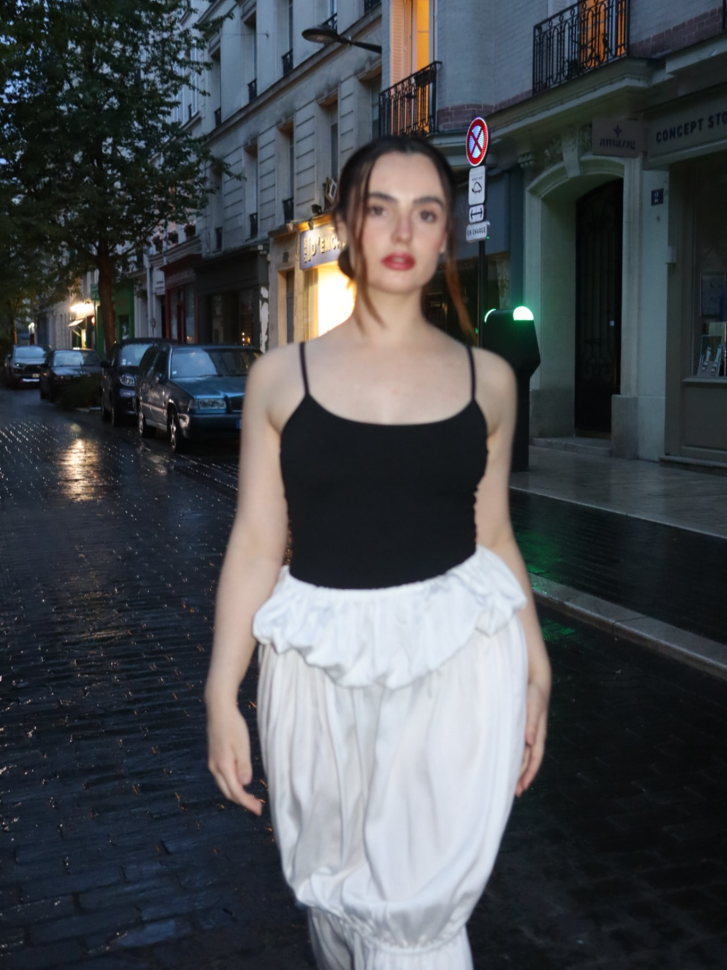 Woman in black top and white skirt walking on a city street at night.