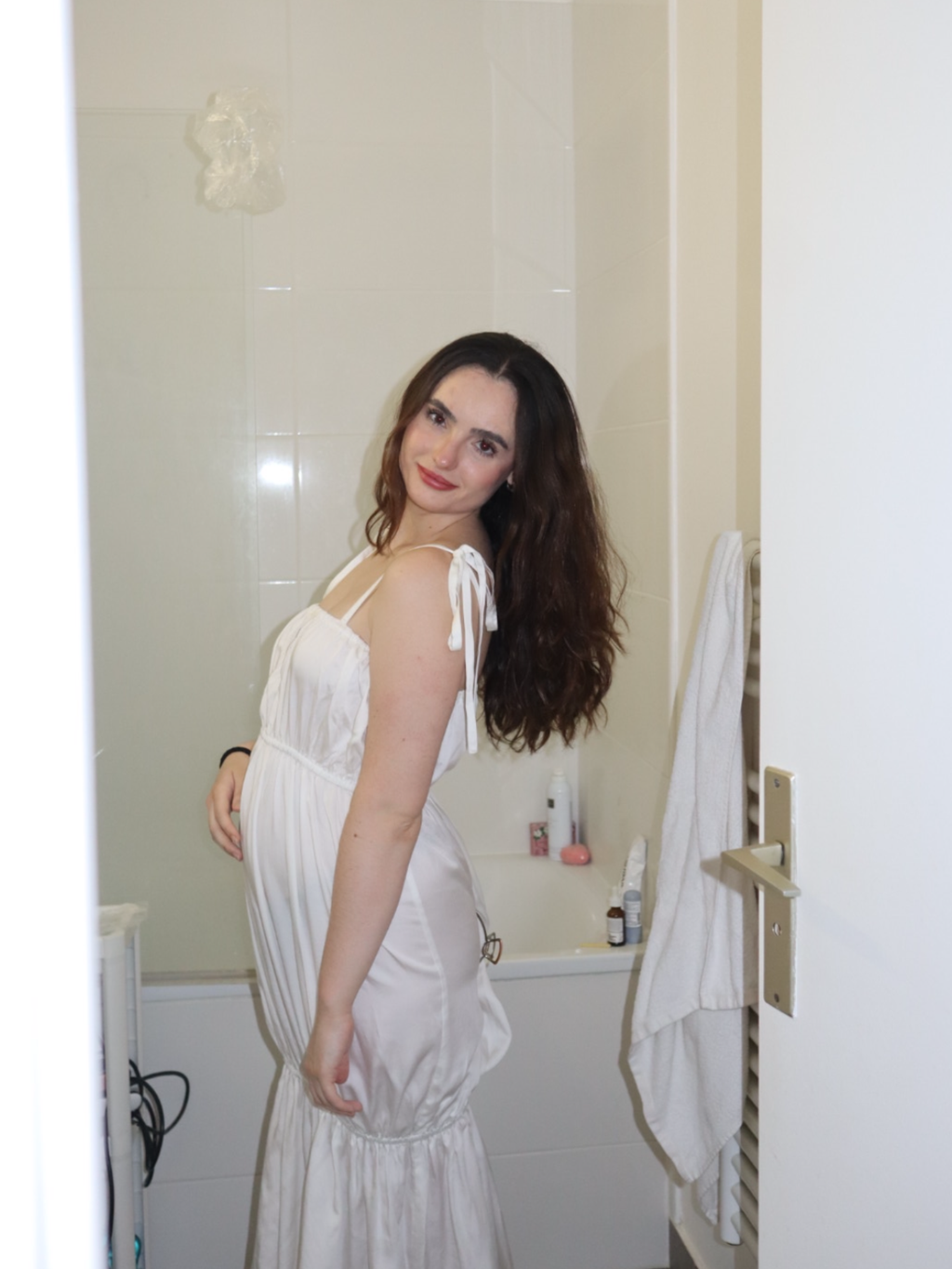 Woman in a white dress standing in a bathroom.