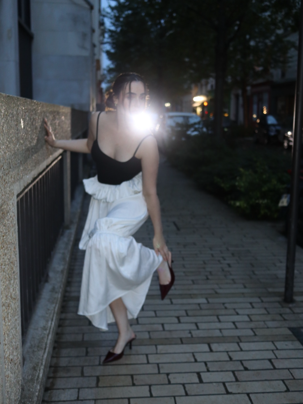 Woman in black top and white skirt standing on a sidewalk at night.