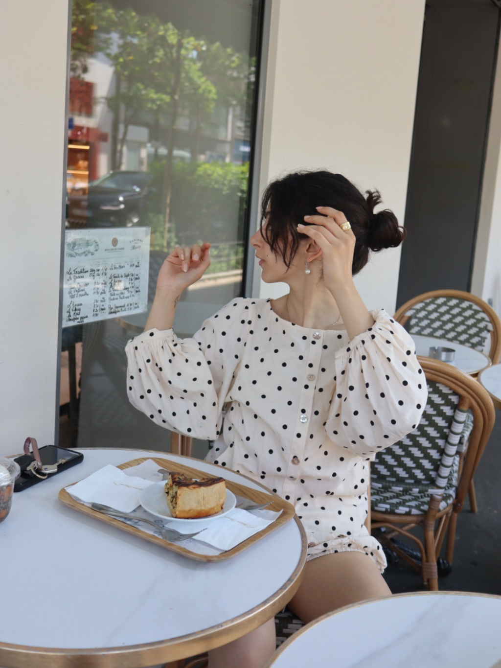 Woman in polka dot blouse sitting at a cafe table with a cake