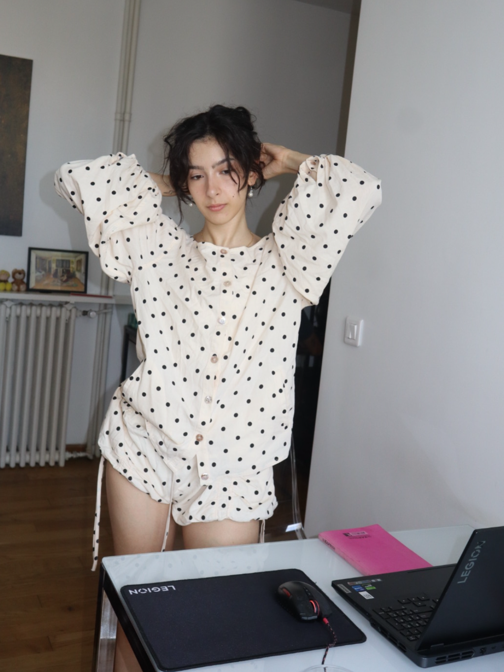 Person wearing a polka dot outfit sitting at a desk with a laptop and mouse.