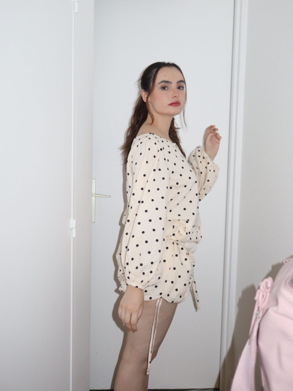 Woman wearing a polka dot outfit standing in front of a white door.