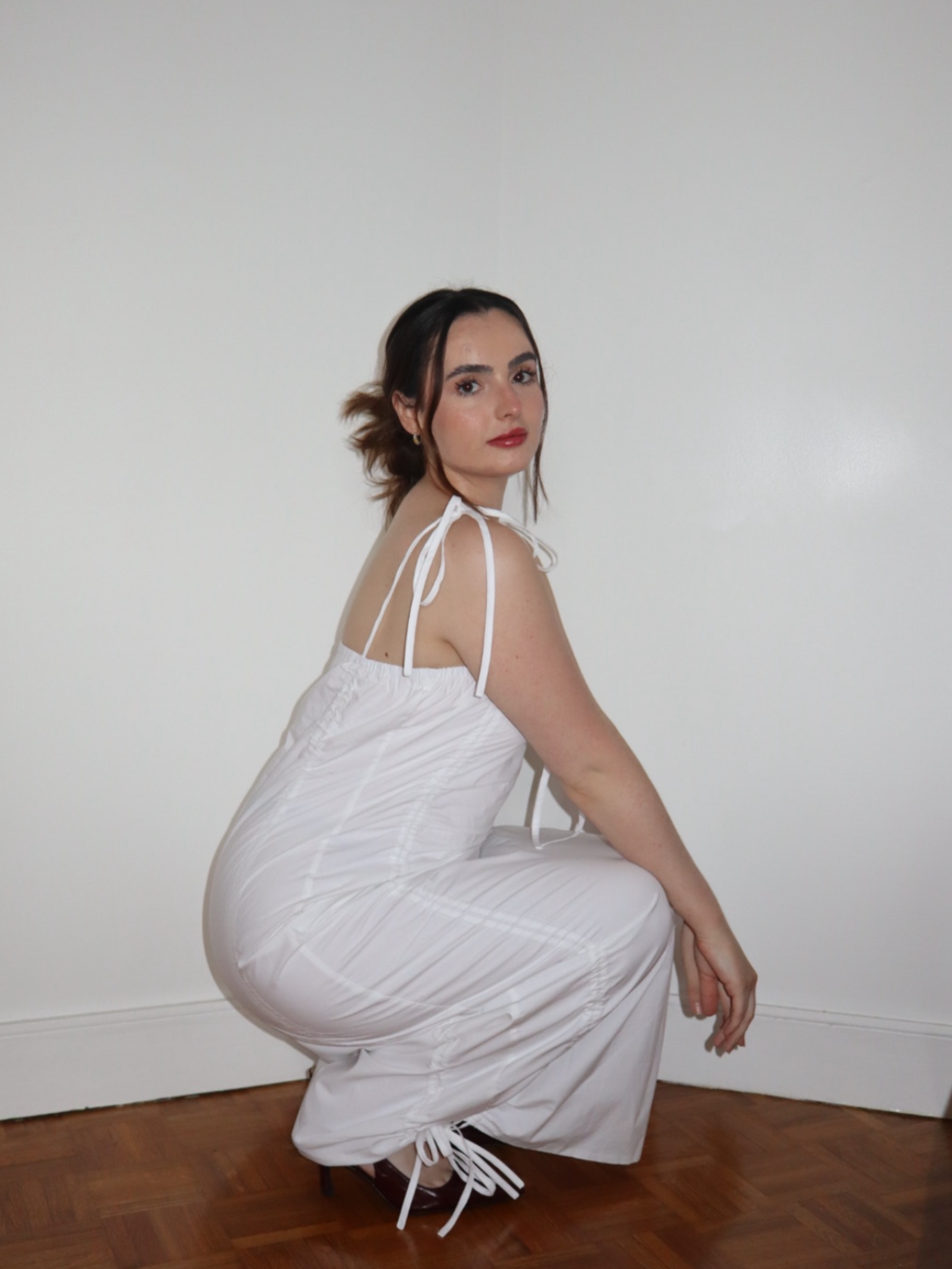 Woman in a white dress sitting on the floor against a plain wall.