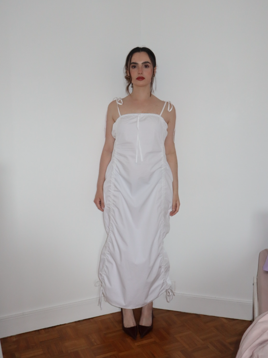 Woman wearing a white dress standing against a plain wall