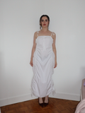 Woman wearing a white dress standing against a plain wall