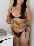 Woman in a red bikini holding a banana in a room with a white door and wooden beam.